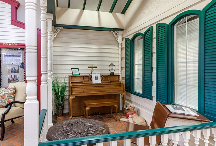 A cozy porch with a piano, surrounded by green shutters and adorned with comfortable decor.