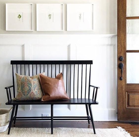 A minimalist entryway features a black bench with decorative cushions and framed wall art.