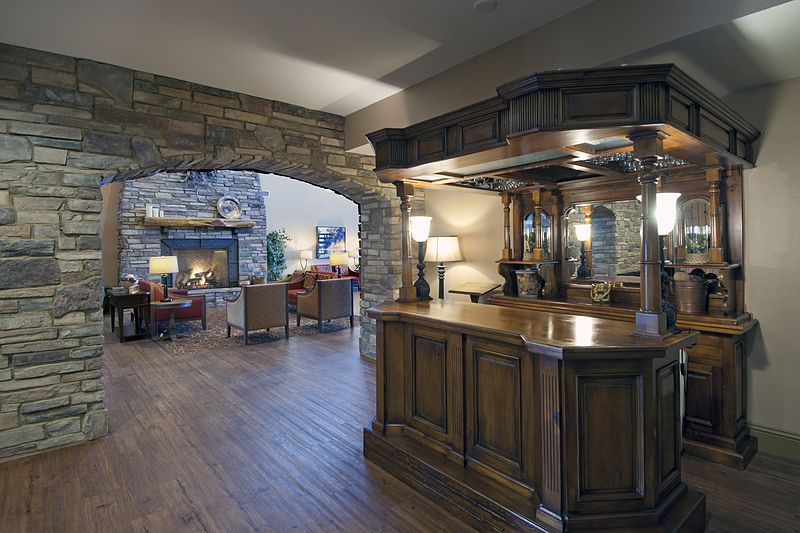 A cozy living space featuring a wooden bar, stone archway, and a warm fireplace.