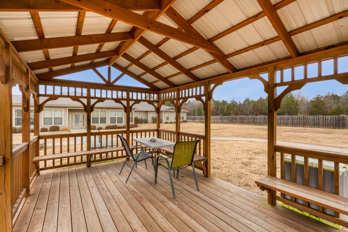 A charming wooden gazebo with a table and chairs, overlooking a spacious yard.