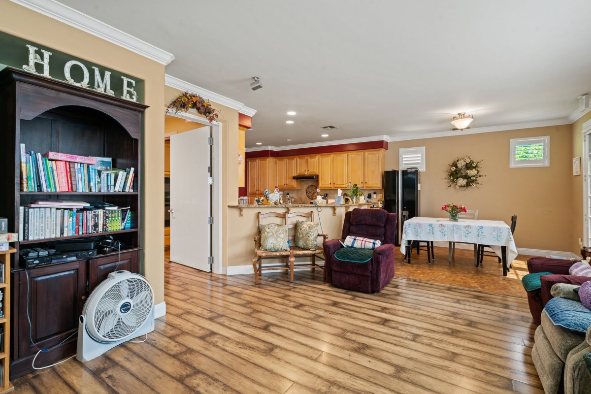 An open-concept living area with a cozy armchair, wooden flooring, and a view into the kitchen.