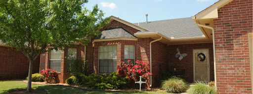 A charming brick house surrounded by lush greenery and blooming flowers.