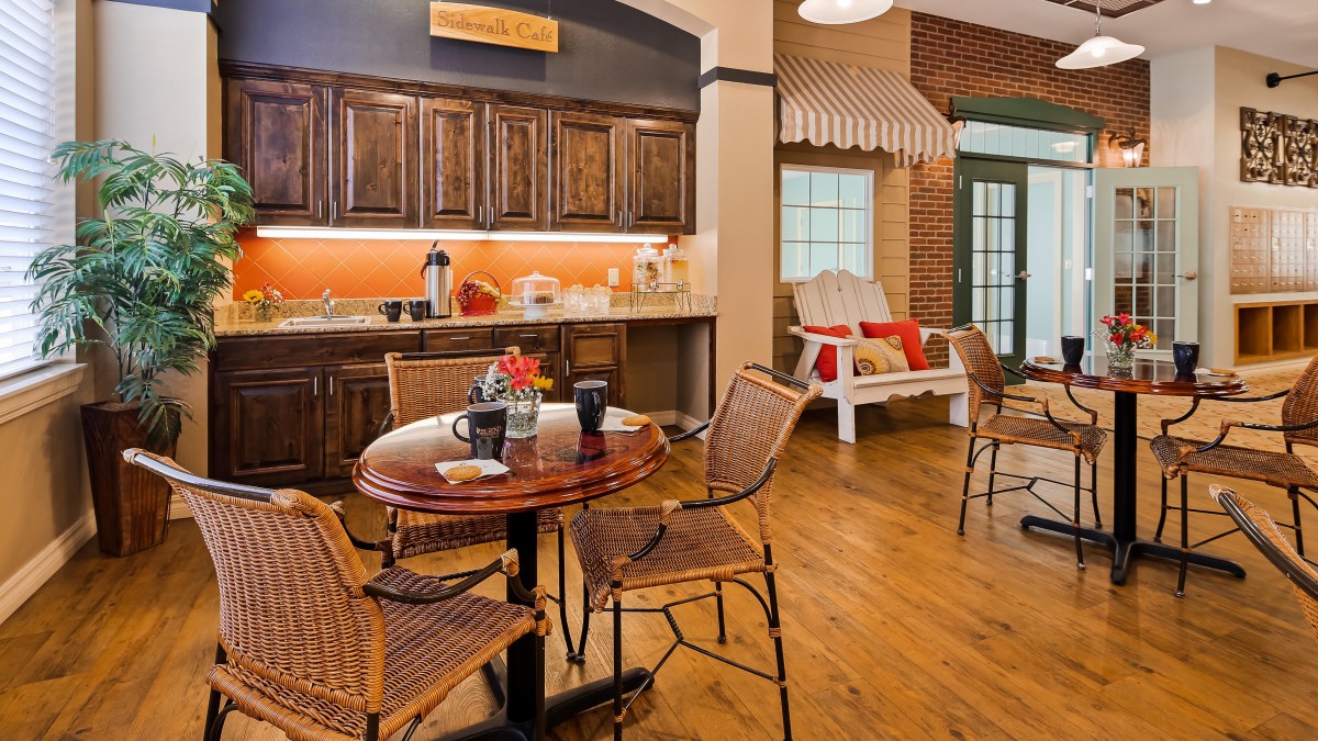 A cozy dining area with wooden furniture and a kitchen setup, featuring coffee mugs and warm lighting.