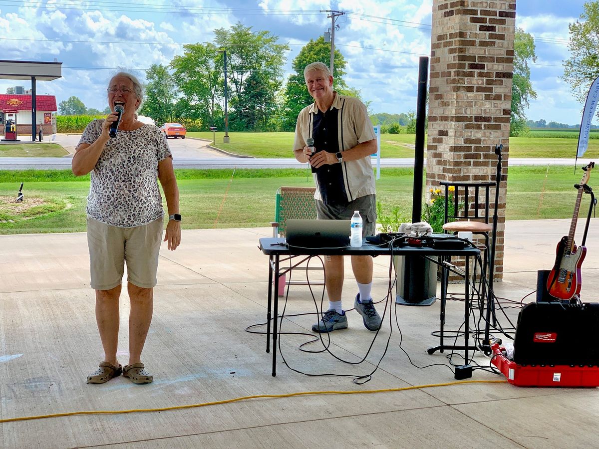 Two people are hosting an event outdoors with electronic equipment on a table.