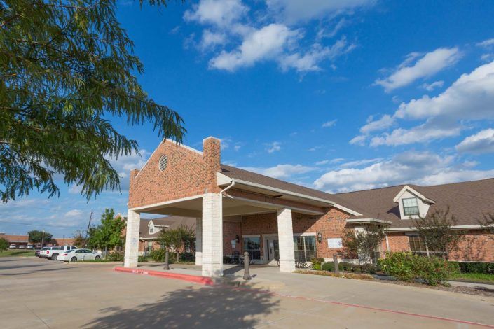 A brick building entrance under a clear blue sky with scattered clouds.