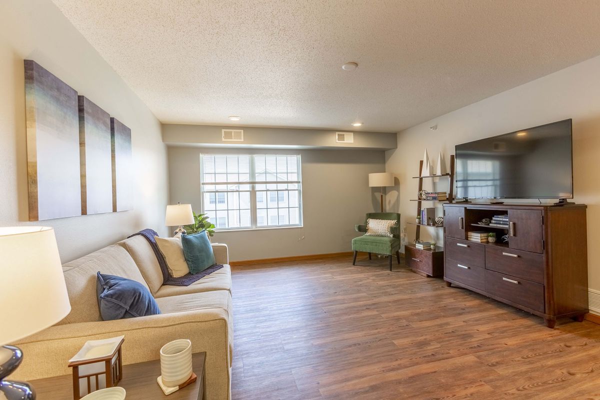 A cozy living room with hardwood floors and modern furniture, featuring a sofa, bookshelf, and large window.