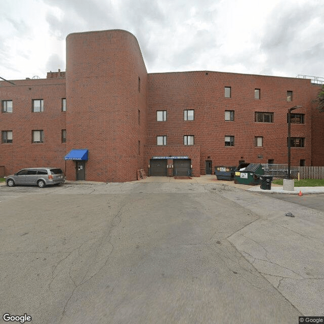 A brick apartment building with a parking lot in front and several cars parked.