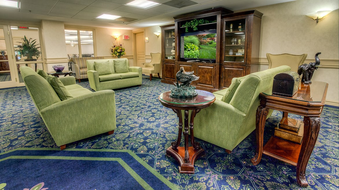 A cozy lobby area with green sofas, a patterned carpet, and a large television.