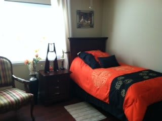 A cozy bedroom with orange bedding and a bedside table near the window.