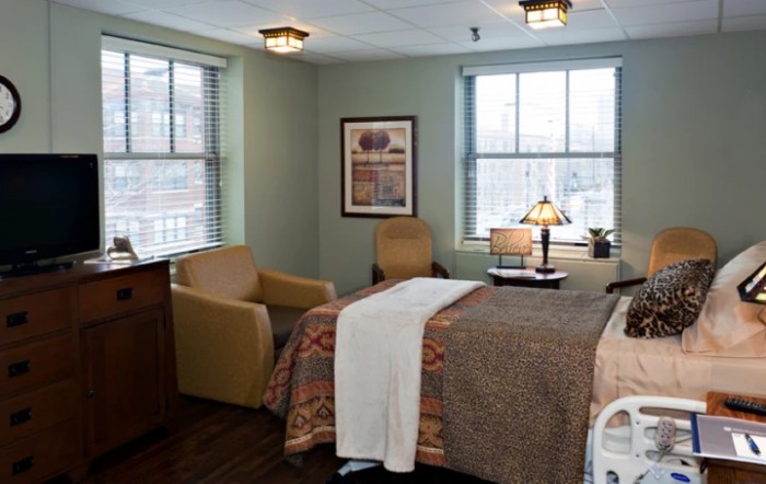 A hospital room with a bed, two chairs, and a lamp near the window.