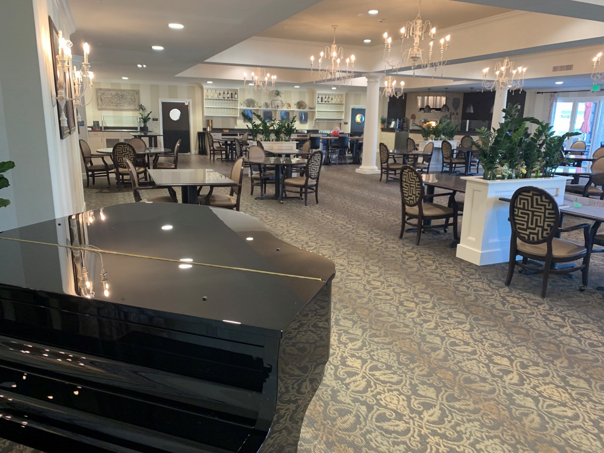 A spacious and elegant restaurant dining area featuring a grand piano and chandeliers.