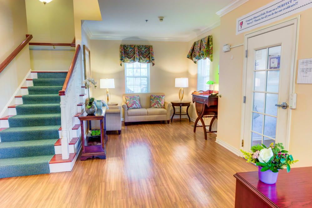 A bright and welcoming living room with wooden flooring, featuring a sofa, desk, and staircase.
