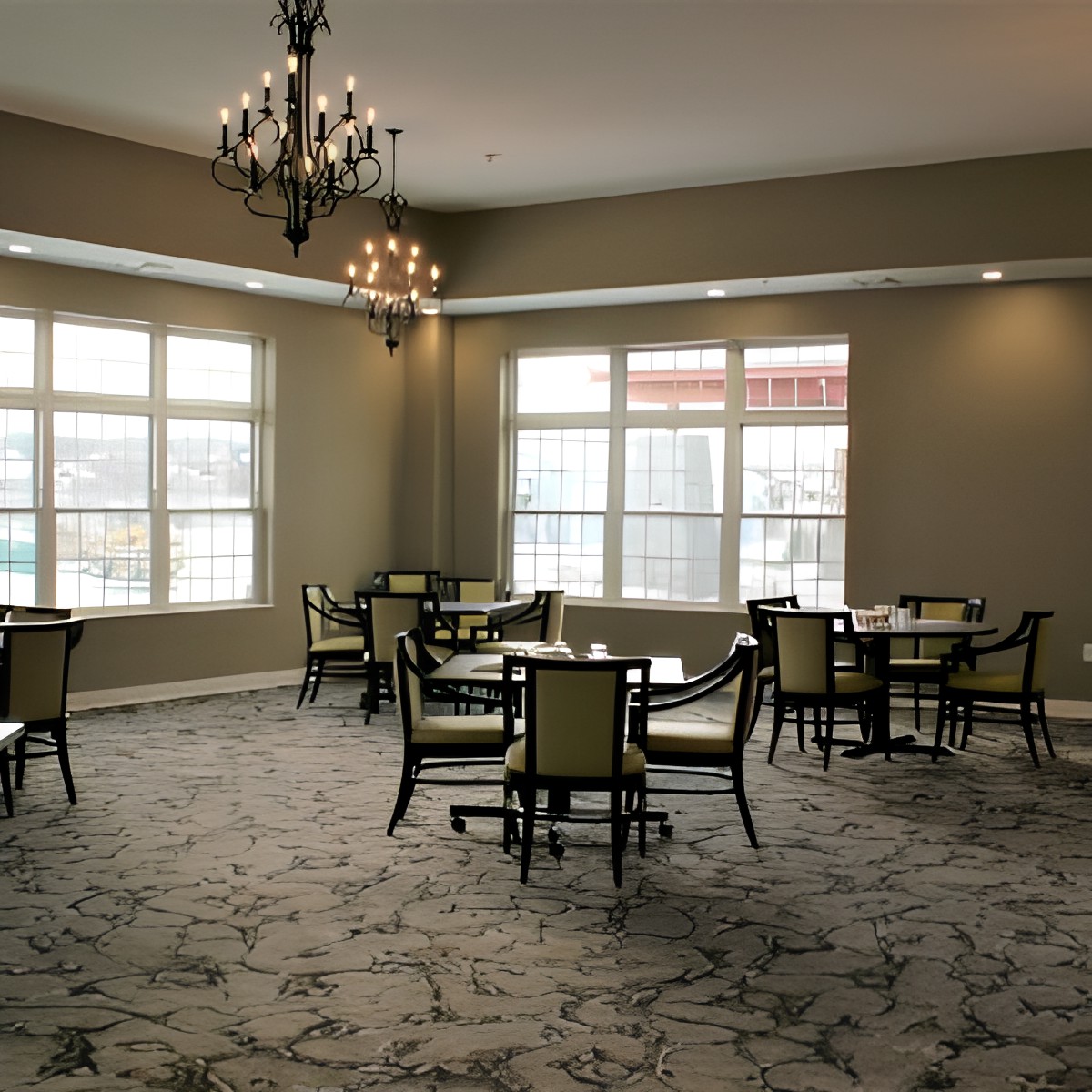 A spacious dining room with multiple tables and chairs, featuring large windows and a chandelier.