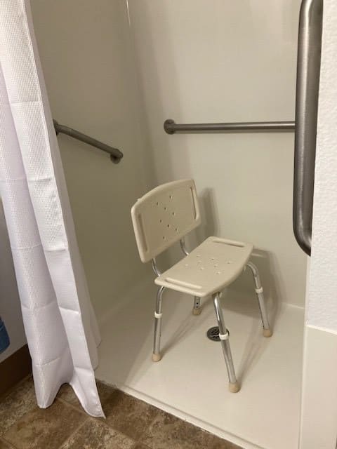 A bathroom shower with a safety chair and grab bars for accessibility.