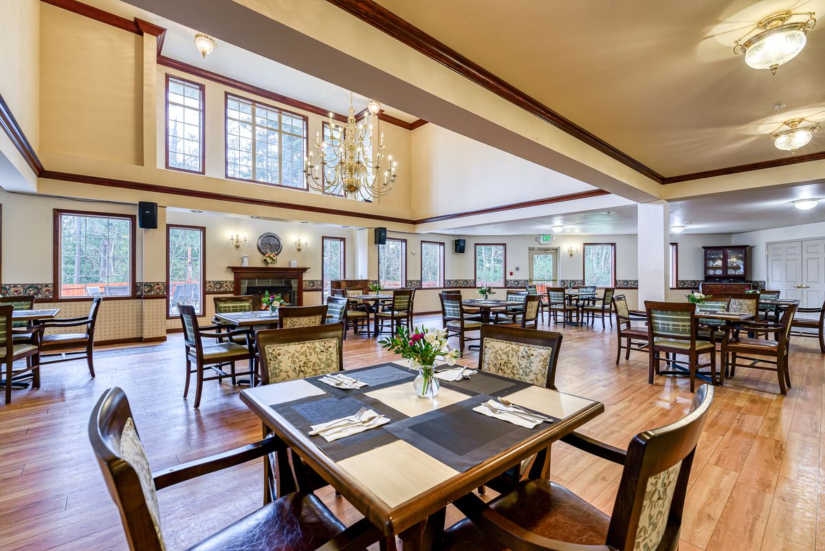 Elegant dining area with stylish furniture and chandeliers, featuring large windows and wooden floors.
