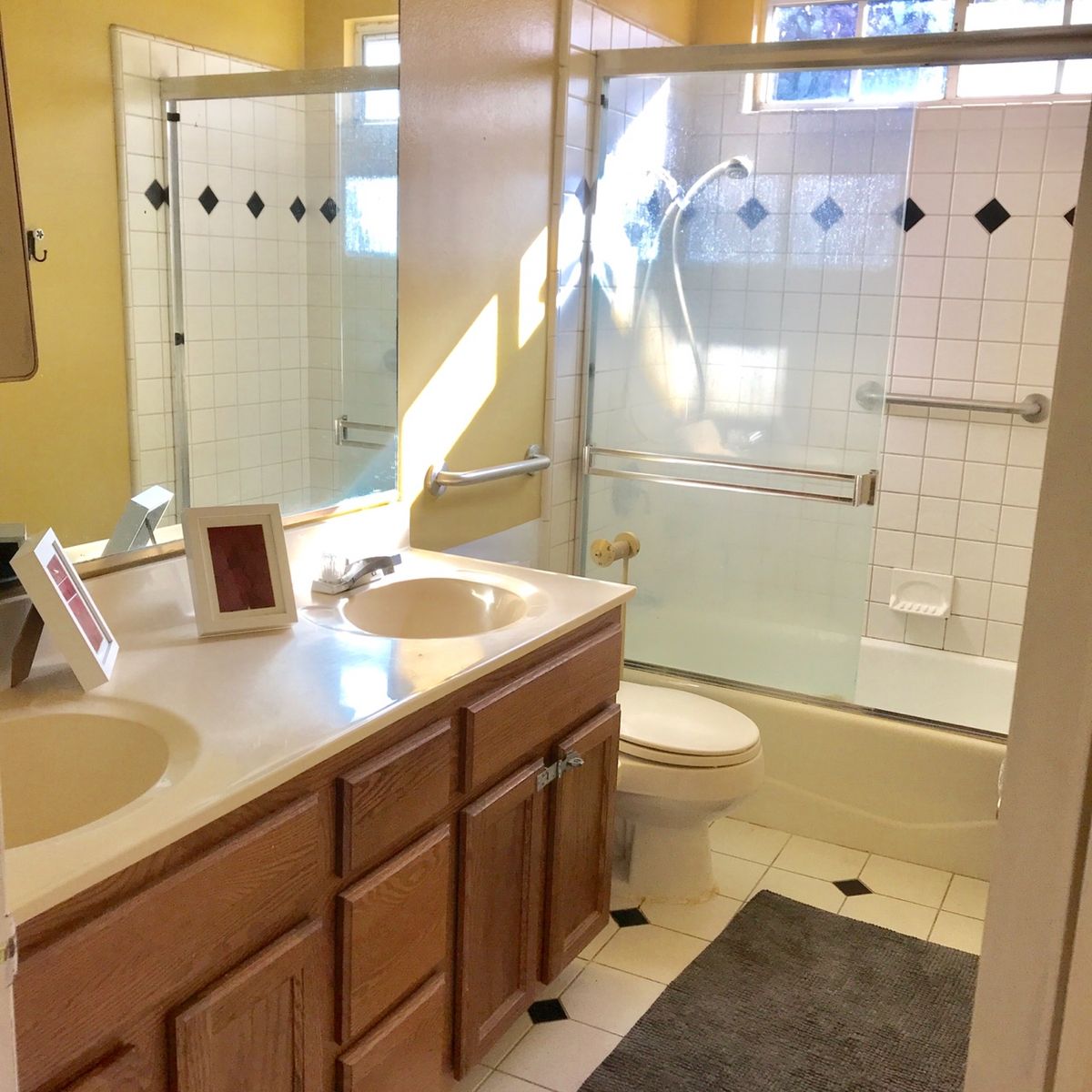 A well-lit bathroom featuring a double sink vanity, glass-enclosed bathtub, and tiled walls.