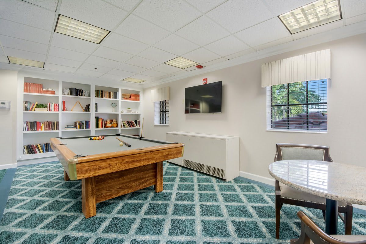 A cozy billiard room featuring a pool table, a wall-mounted television, and bookshelves.