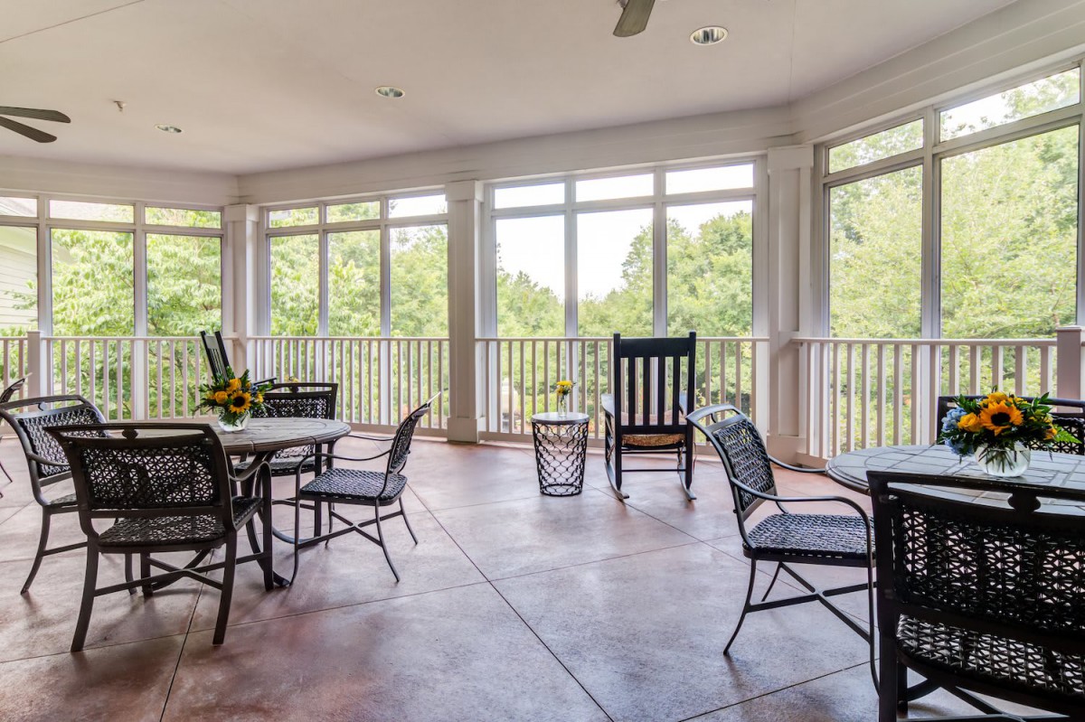 A spacious patio with comfortable seating and large windows overlooking a lush green landscape.