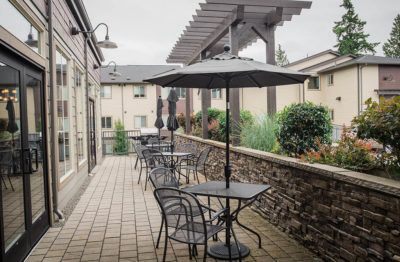 An outdoor patio with tables and chairs under umbrellas on an overcast day.