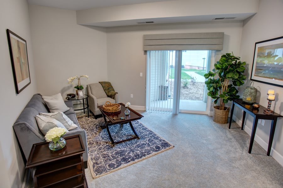 A cozy living room with modern decor, featuring a sofa, armchair, coffee table, and large window with curtains.