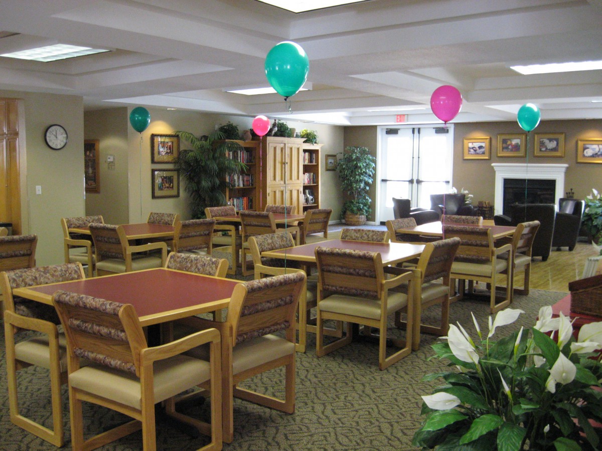 A decorated dining room with tables and chairs, featuring colorful balloons hanging from the ceiling.
