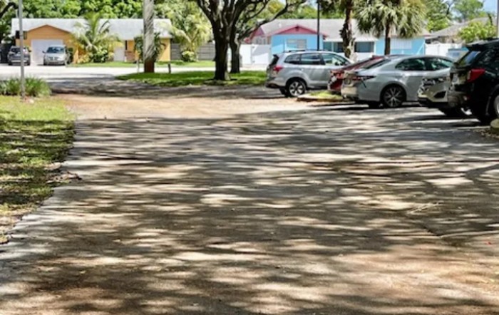 A sunny parking lot with cars and tree shadows.
