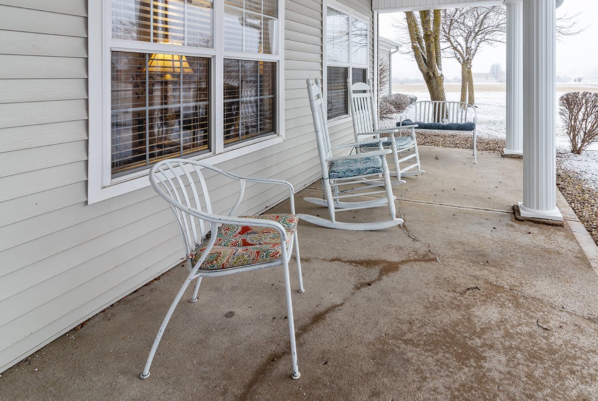 A cozy porch with a rocking chair and metal chairs overlooking a scenic view.