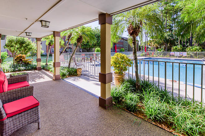 A covered patio overlooking a pool with tropical plants and a seating area.