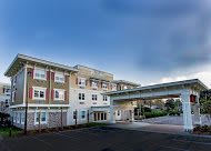A modern healthcare facility with an extended covered driveway and a cloudy sky backdrop.