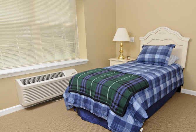 A cozy bedroom with a single bed and plaid bedding next to a nightstand and lamp.
