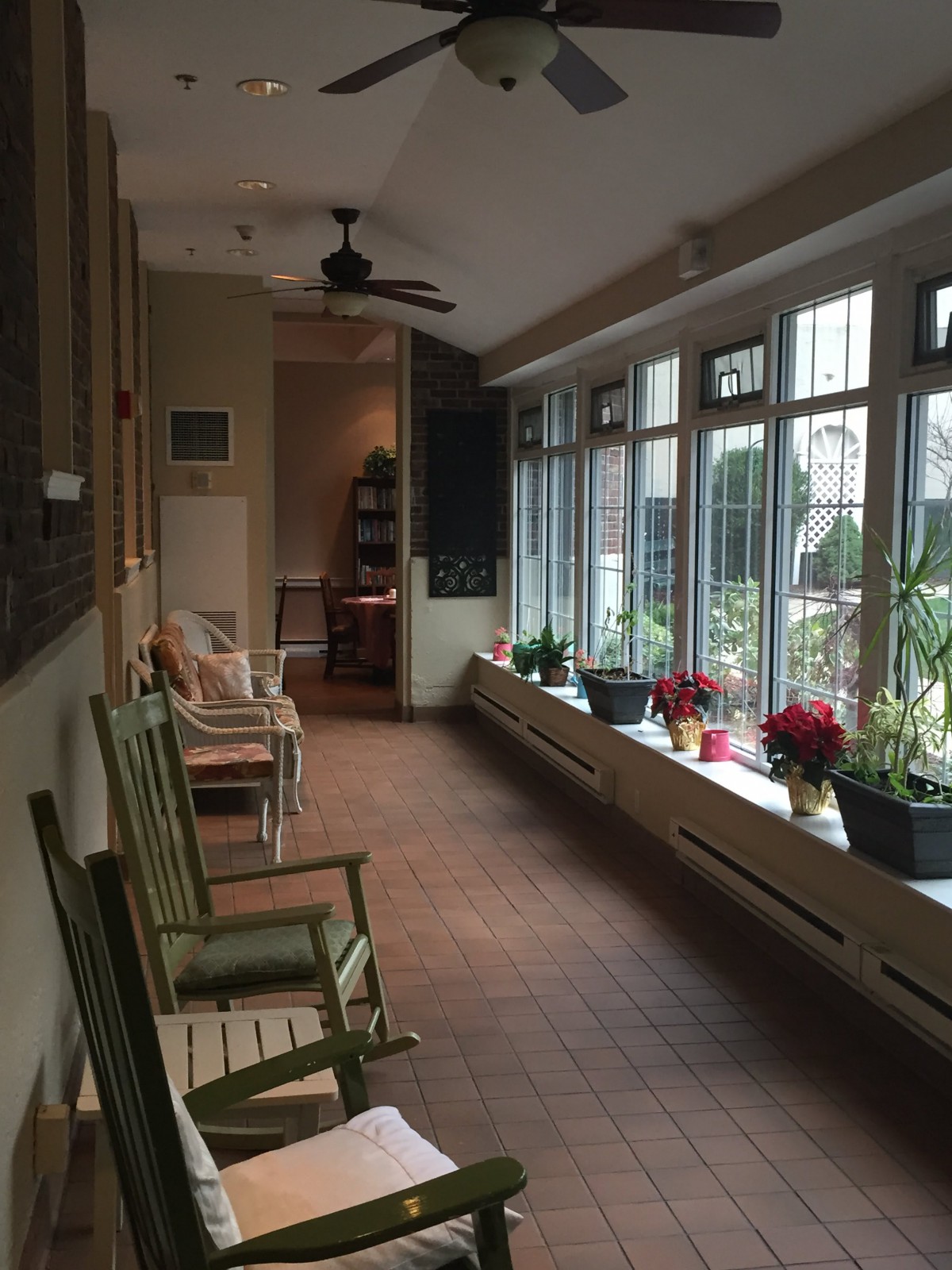 A cozy sunroom with rocking chairs and potted plants by large windows.