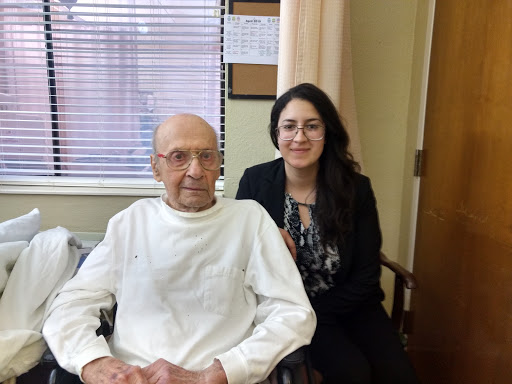 A caregiver poses for a photo with an elderly man in a hospital setting.