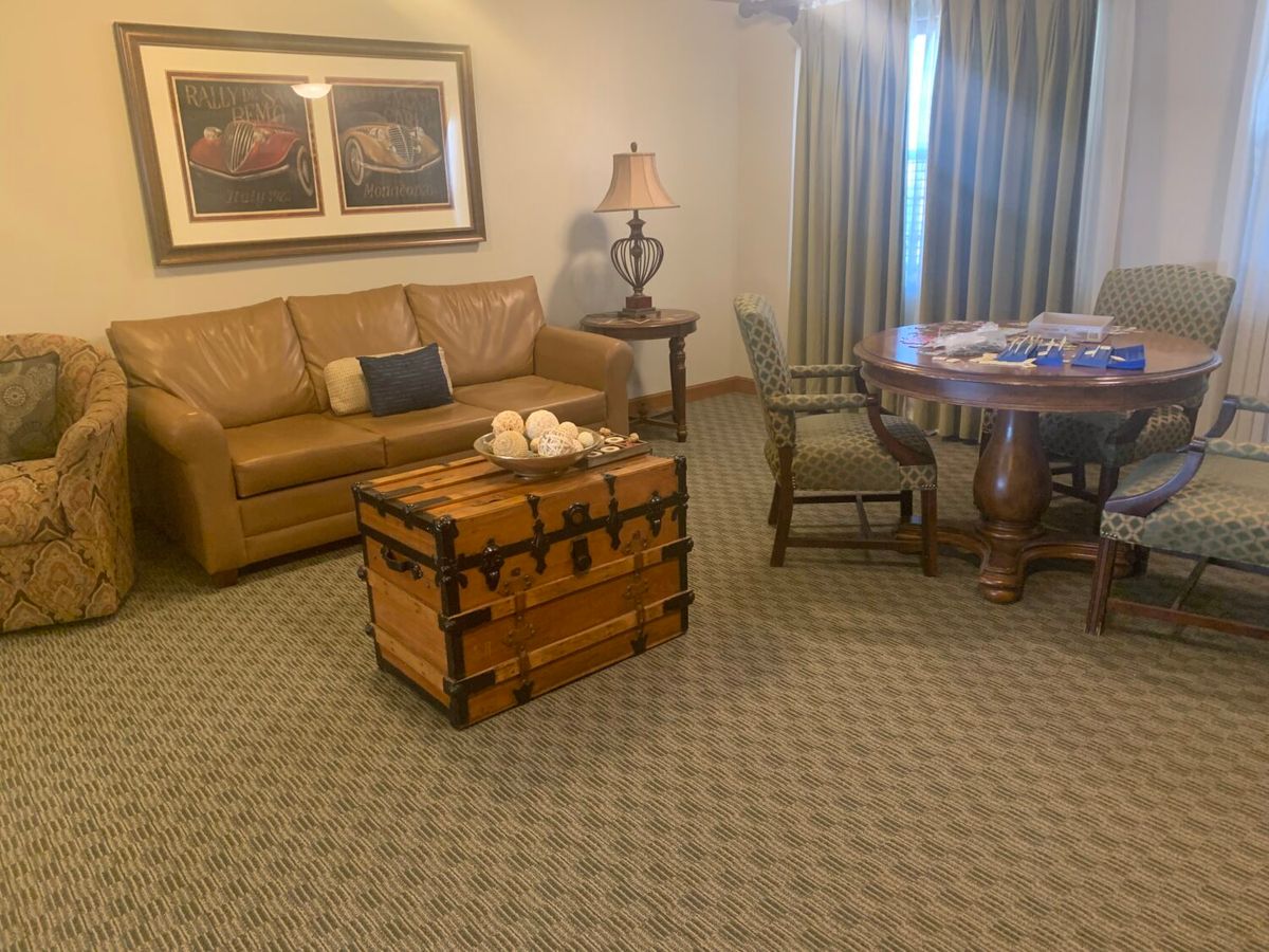 A cozy living room with a leather sofa, wooden chest, round table, and chairs.