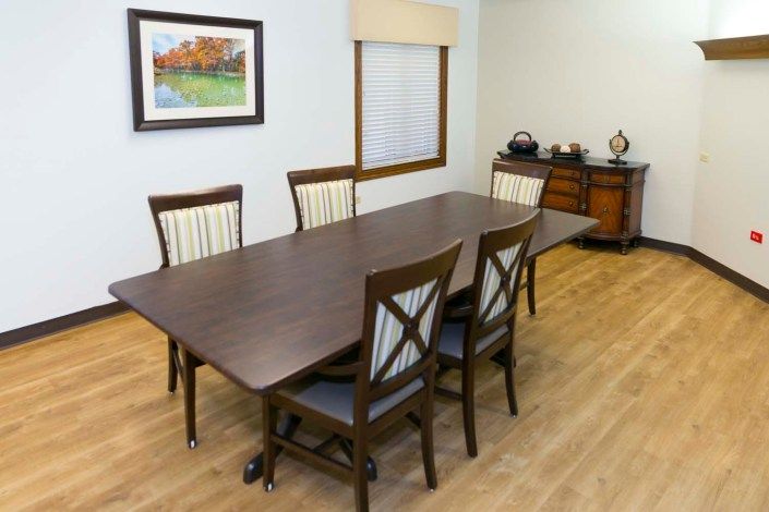 A dining room with a wooden table and six chairs, featuring a wooden floor and wall art.