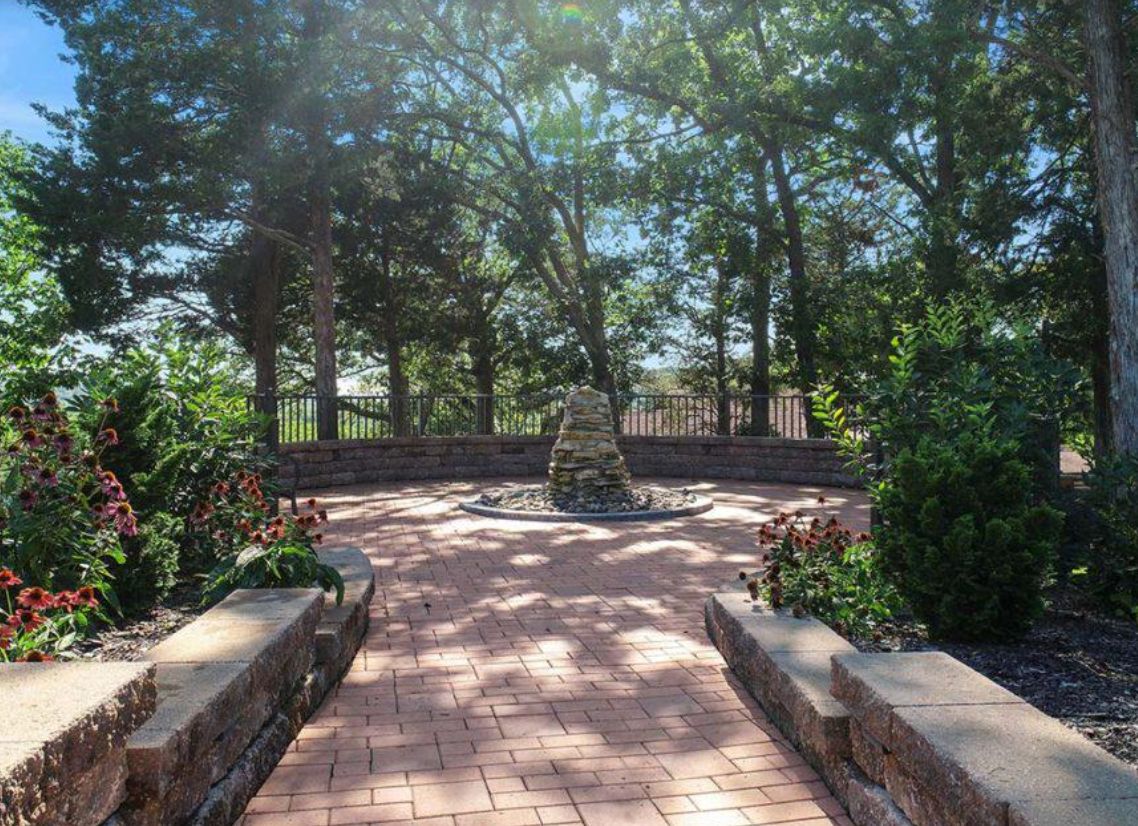 A peaceful garden with a brick pathway leading to a stone structure surrounded by trees.
