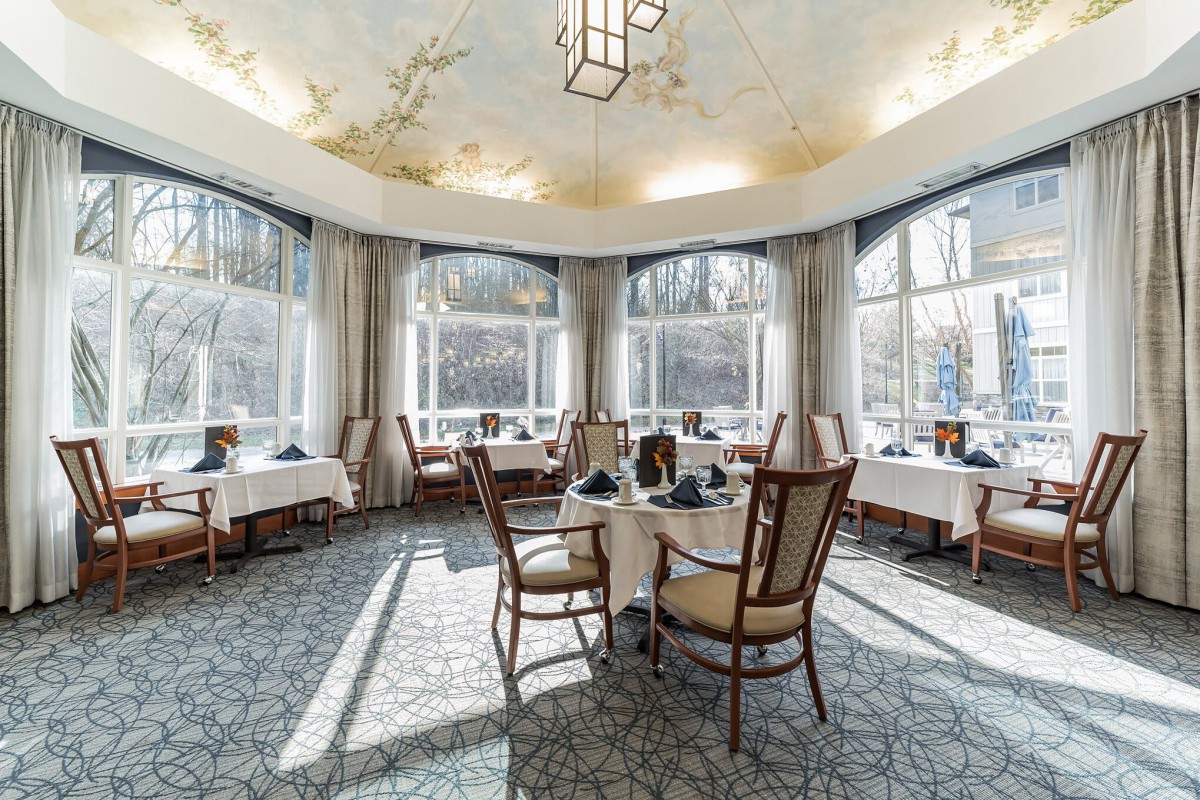 An elegant dining area with large windows allowing sunlight to brighten the room, featuring neatly arranged tables and chairs.