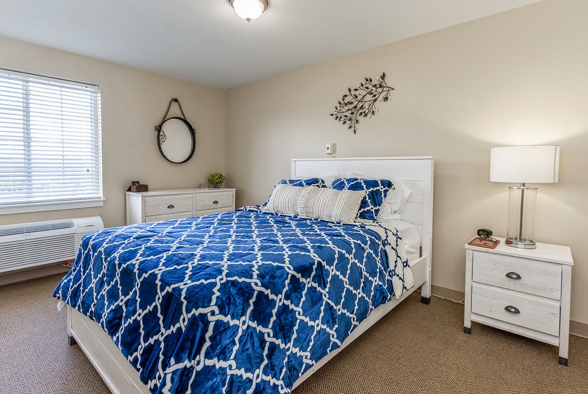 A cozy bedroom featuring a bed with blue patterned bedding, a white dresser, and decorative wall elements.