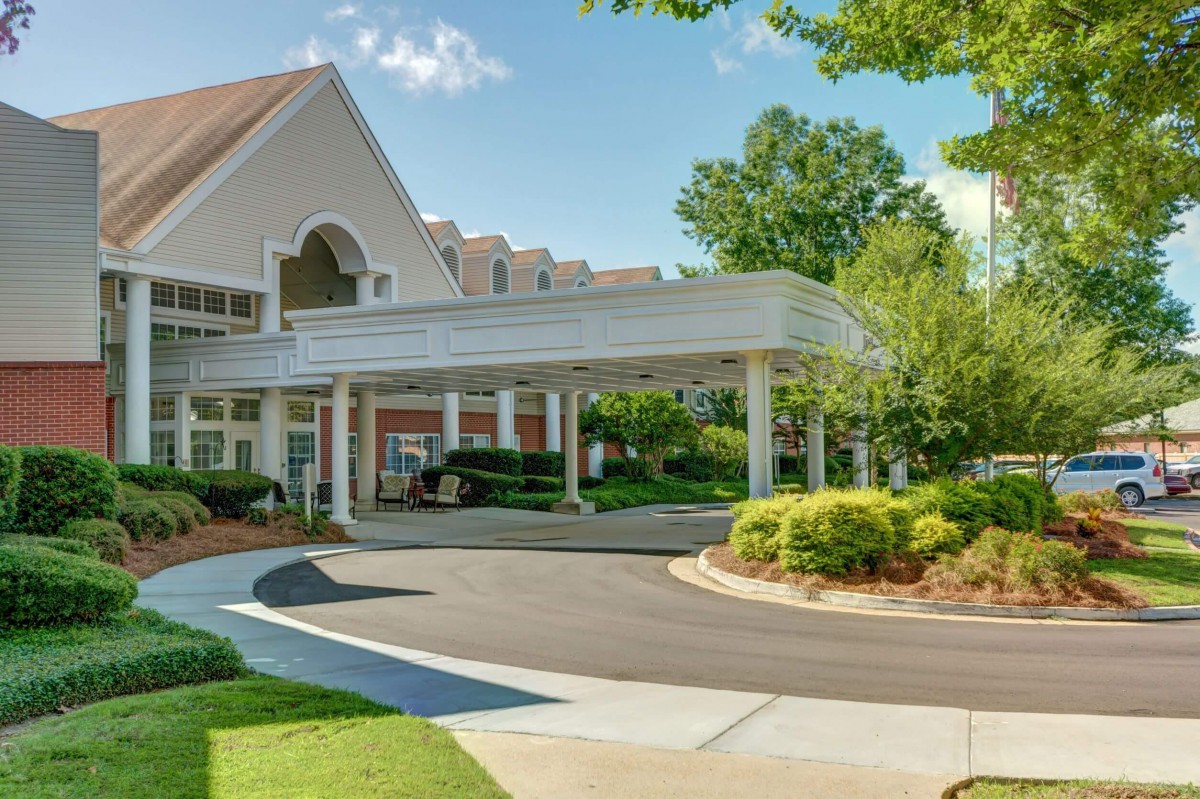 A building entrance with a covered driveway surrounded by greenery.