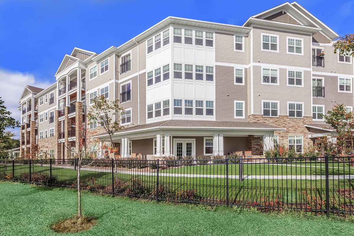 A modern apartment complex with well-maintained landscaping and a black metal fence.