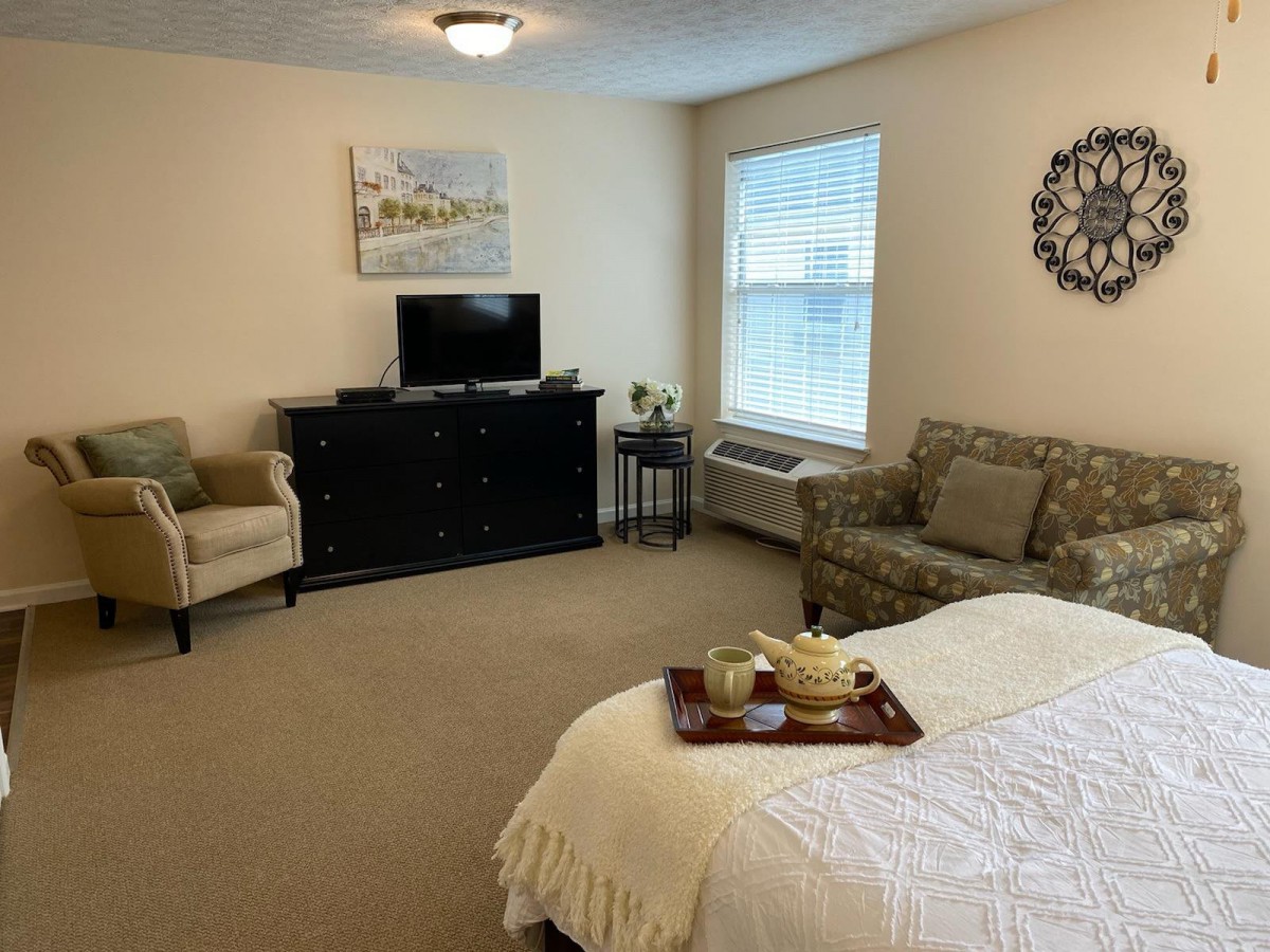 A cozy, modern bedroom with a bed, TV, armchairs, and wall decor.