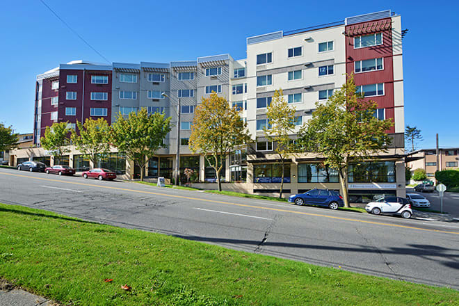 A colorful residential building along a street with parked cars and trees.