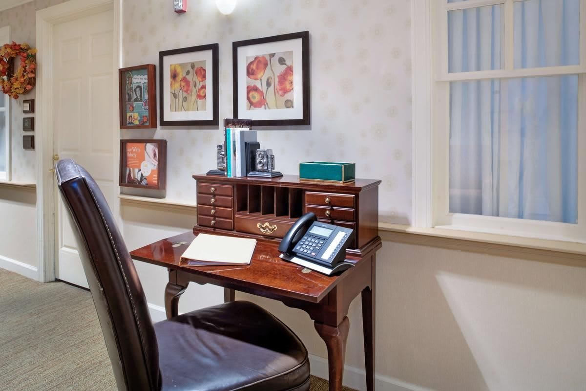 A vintage wooden desk with a telephone and books, complemented by framed wall art in an office setting.