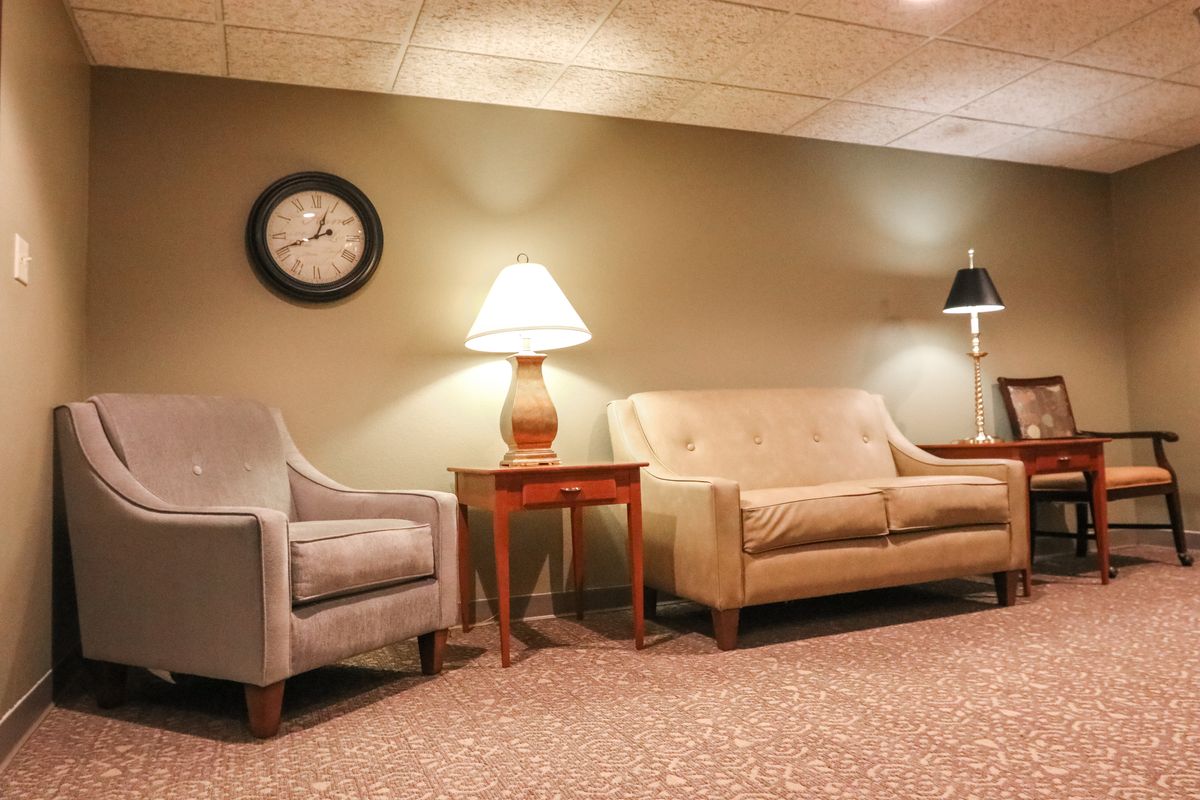 A cozy living room with a sofa, chair, lamps, and a wall clock.