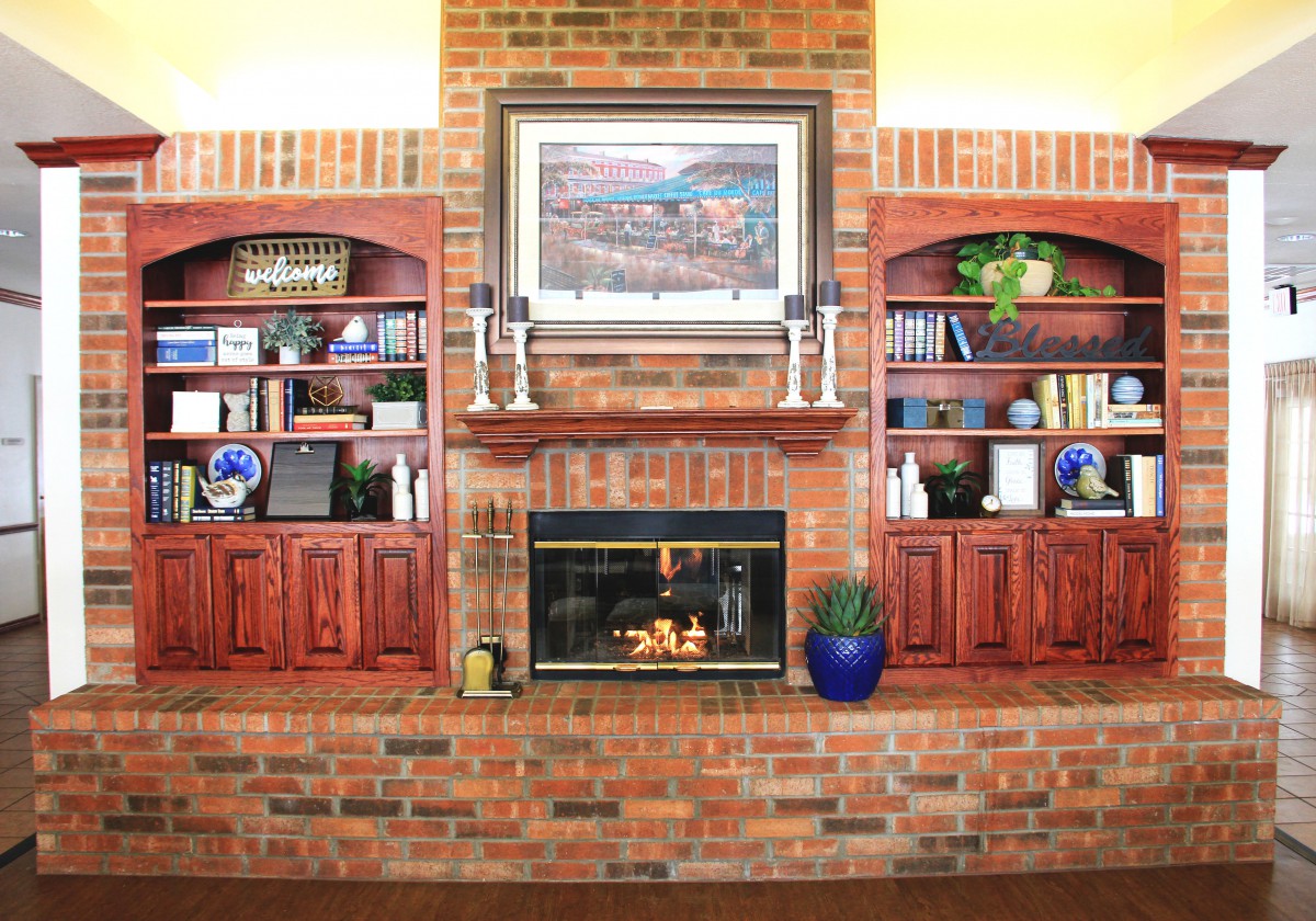A cozy living room with a brick fireplace flanked by built-in bookshelves and decorated with artwork above.