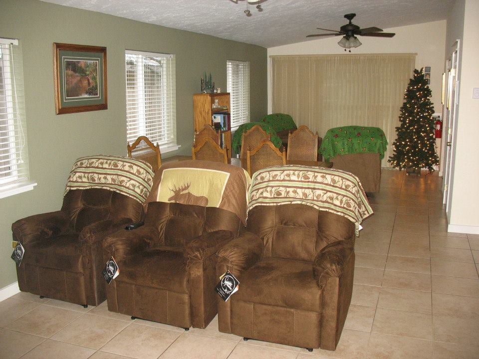 A cozy living room with multiple recliner chairs and a large television, decorated with a Christmas tree.