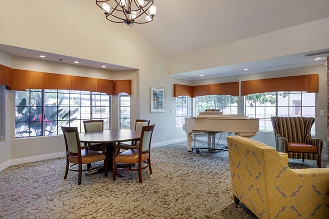 A spacious living area featuring a round dining table and chairs, a grand piano, and large windows providing natural light.