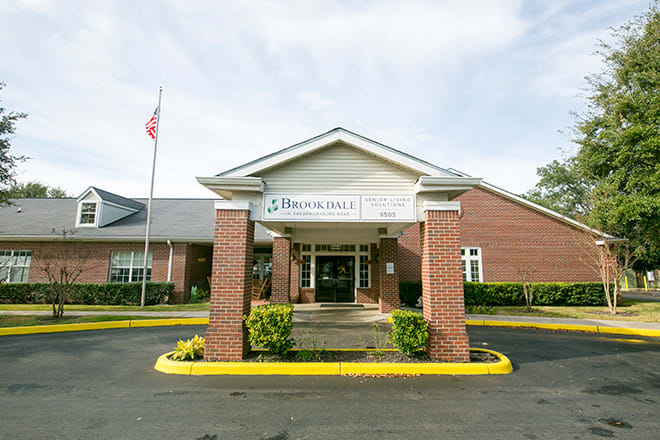 The entrance of a brick building with a flagpole and landscaping.