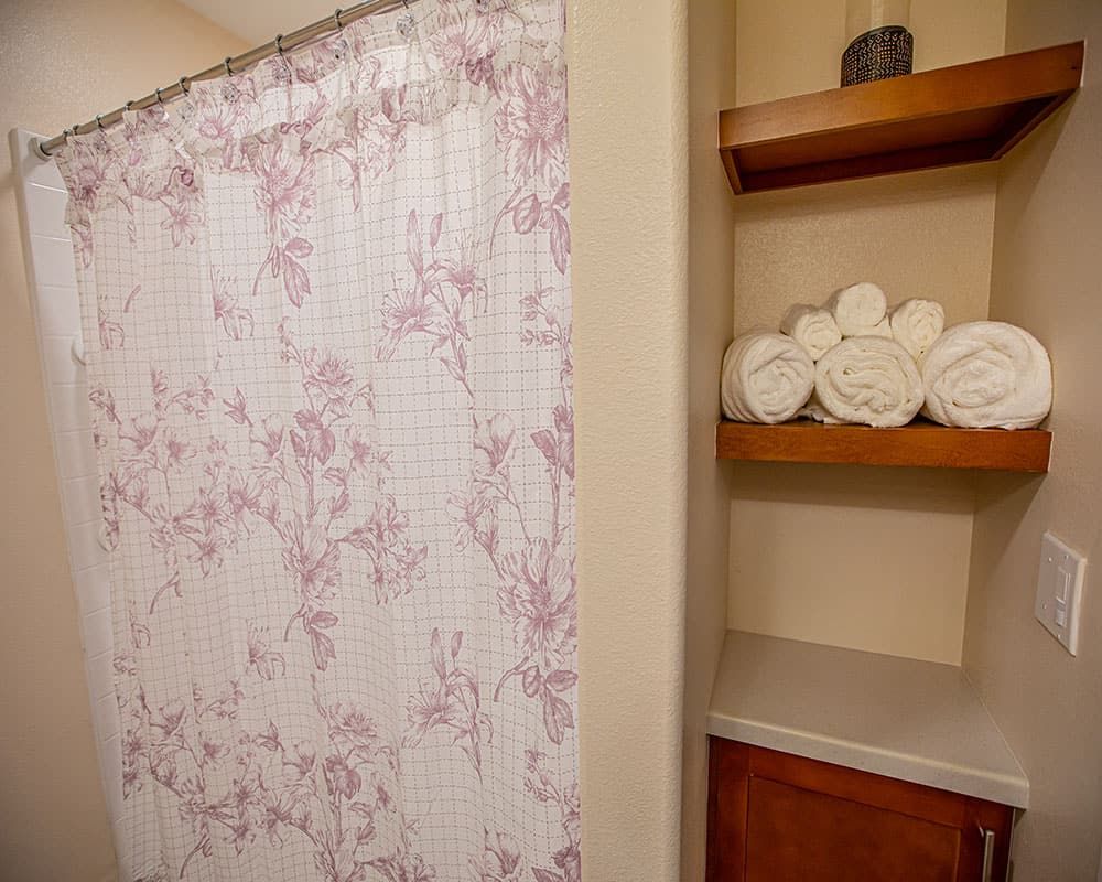 A bathroom with a floral shower curtain and neatly arranged towels on shelves.
