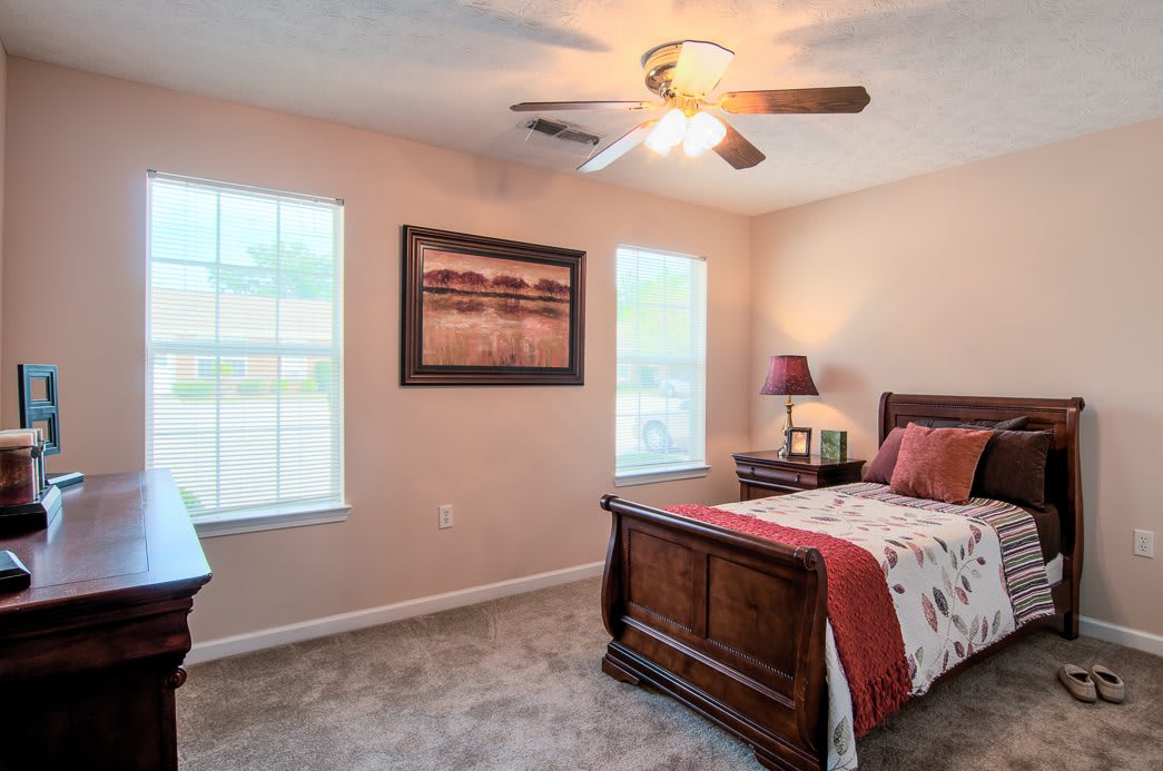 A cozy bedroom with a single bed and ceiling fan, featuring natural light from two windows.