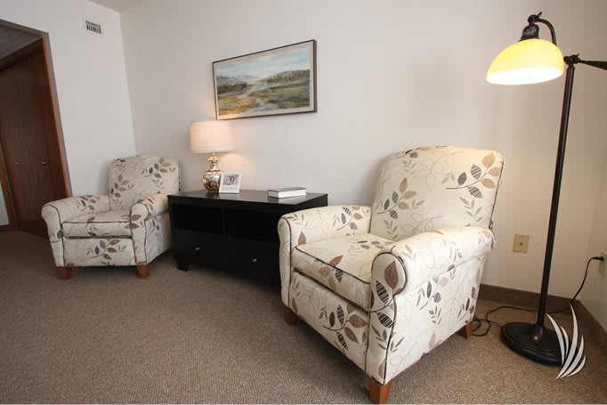 A cozy living room setup featuring two floral armchairs, a side table with a lamp, and wall art.